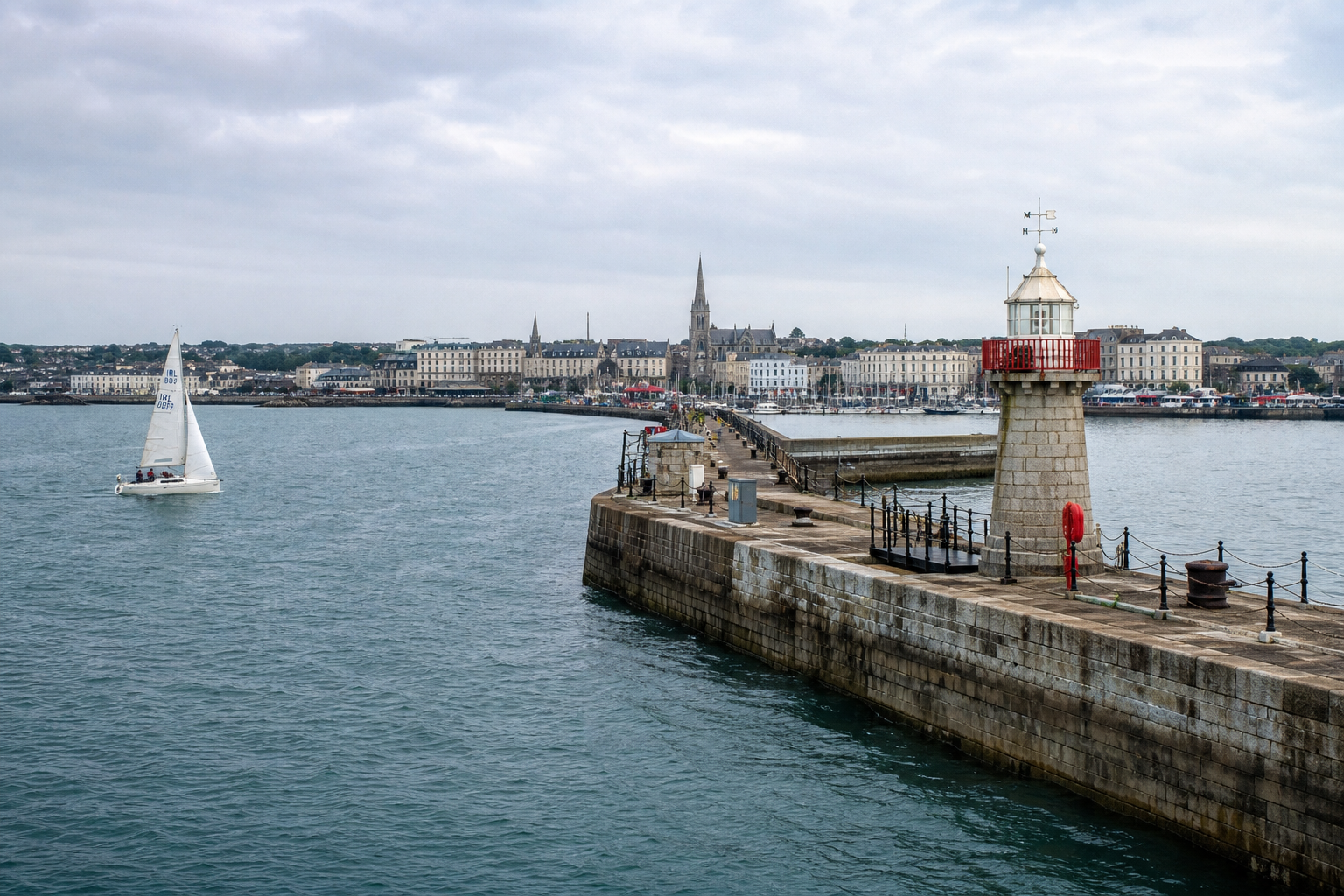 Dún Laoghaire harbour at dusk — the East Pier curving out into a calm summer evening, lighthouse silhouetted, the bandstand on the seafront just visible